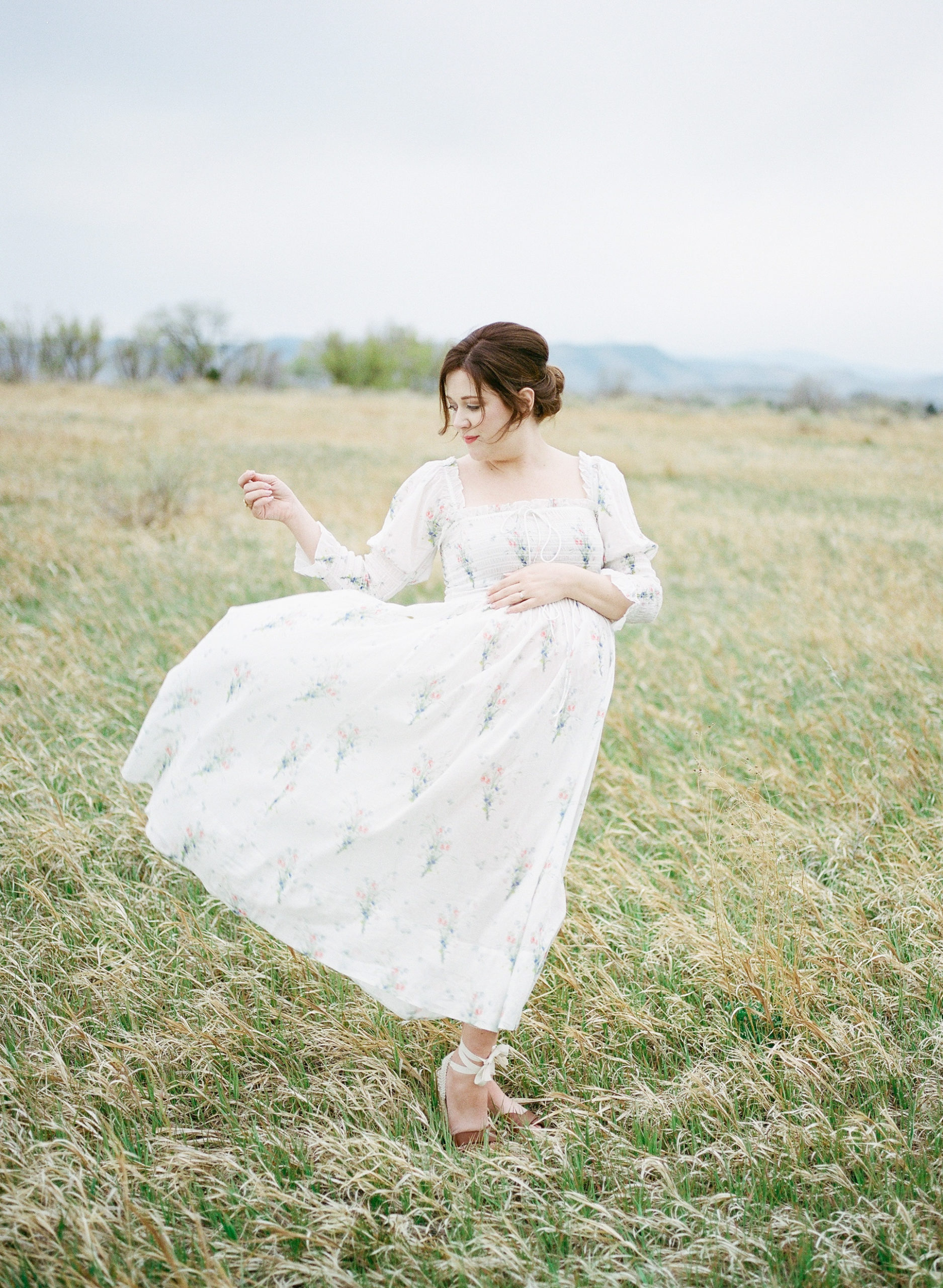 Pregnant Mama in a field with mountain views in the distance. Lots of movement shown in her hand and dress